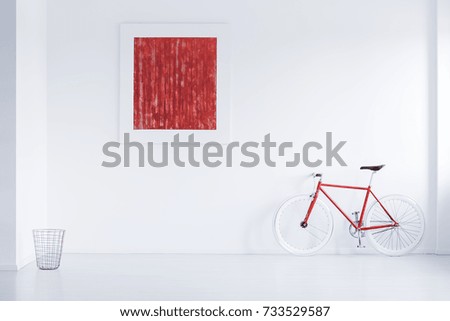 Metal basket placed in the corner of white room with red poster and bike