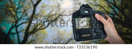 Cropped hand of photographer holding camera  against green trees in the forest