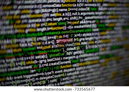 Macro photo of computer screen with program source code and highlighted SPYWARE inscription in the middle. Script on the screen with virus in it. Cyber security concept. Technology background.