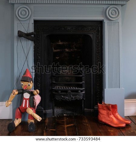 Victorian era fireplace surround by blue wall, with puppet, quirky orange ankle boots and butterfly pictures. Photographed October 2017.