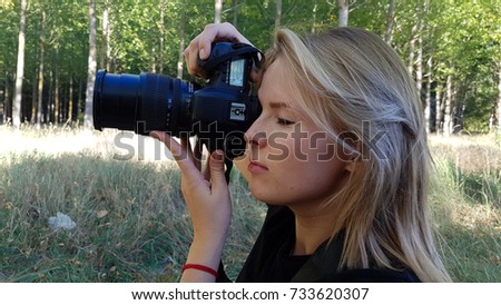 Blond girl making photos with camera reflex. Girl photographing in bosuqe
