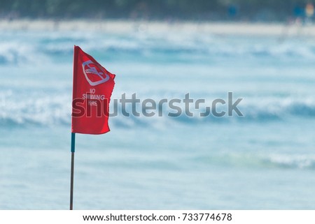 Red flag sign standing against strong wind on the beach warning and prohibiting tourists not swimming due to dangerous big wave and thunderstorm in monsoon season. 
Red warning flag.