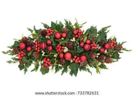 Christmas table decoration with red bauble decorations, holly, ivy, mistletoe, fir and pine cones on white background.