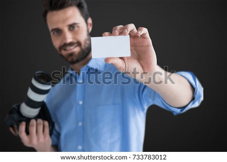Happy man showing identity card while holding camera against grey vignette