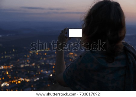 young girl takes pictures on a smartphone lights the night city located in the mountains