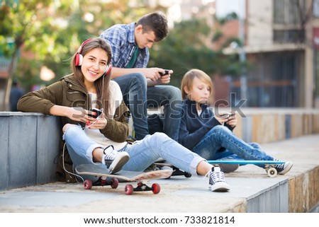 Teenage males and smiling girl relaxing with mobile phones outdoor
