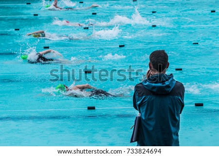 male swimming coach standing by the swimming pool in the rain watching swimmers racing by, good for coaching or training concept Royalty-Free Stock Photo #733824694