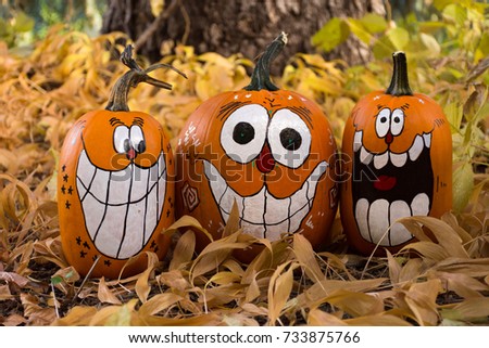 Close up of three decorated pumpkins that are painted with smiles, big teeth and oval eyes. Photographed among dried leaves. Shallow depth of field.