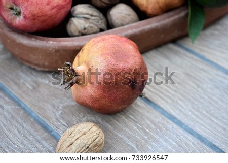 Green tangerine, pomegranate, apple and walnut on a clay plate with a ceramic background