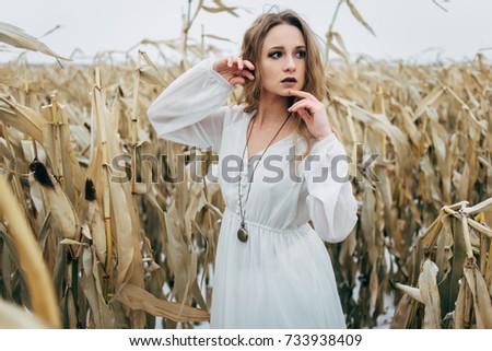 A beautiful girl stands in a dress in an unharched field of corn in winter. tonic