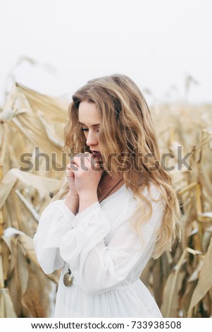 A beautiful girl stands in a dress in an unharched field of corn in winter. tonic