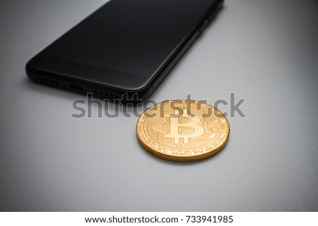 a bitcoin and smart phone on a white isolated surface