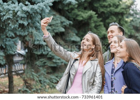 A group of smiling friends taking a mobile phone are photographed outdoors.