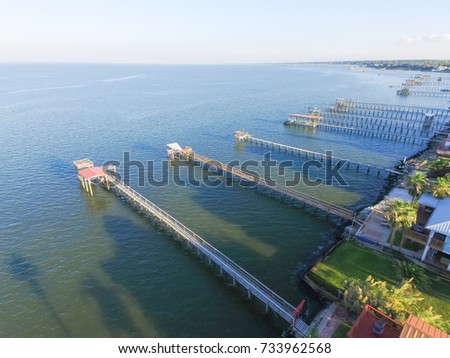 Aerial view three-story waterfront vacation home with fishing piers stretching out over the Galveston Bay in Kemah city, Texas, USA. Bird eye view of Kemah Lighthouse District at sunset.