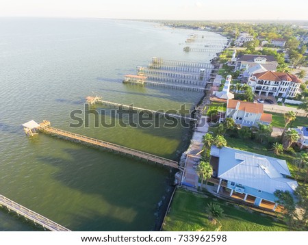 Aerial view three-story waterfront vacation home with fishing piers stretching out over the Galveston Bay in Kemah city, Texas, USA. Bird eye view of Kemah Lighthouse District at sunset.