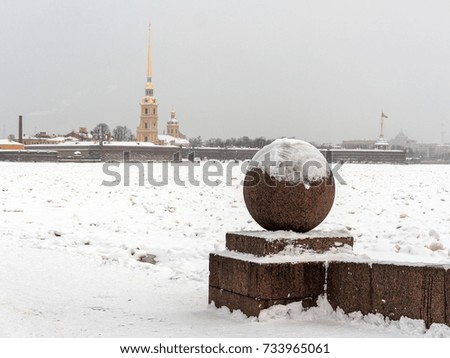 Landmark in Saint Petersburg, Russia: the Spit of Vasilievsky Island  by a winter day with granite sphere, Peter and Paul fortress and cathedral at the horizon and the Neva river covered by  ice.