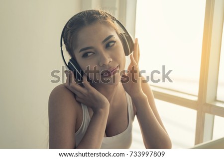 Asian women listen to music with wireless headphones by the window.