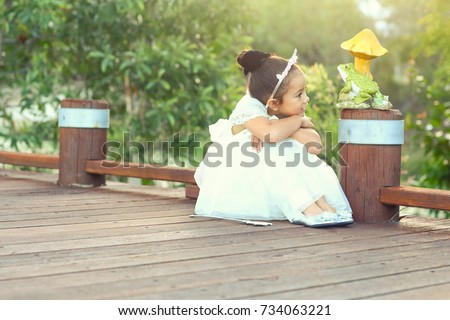The cute little princess and the frog prince on the bridge in the beautiful light.