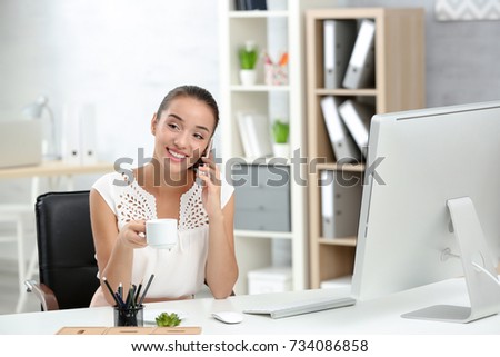 Beautiful young woman speaking by mobile phone in office