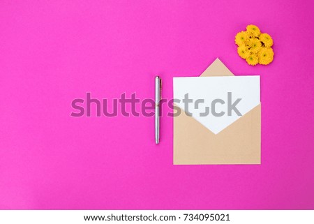 Romantic pink background of an isolated blank card, envelope, pen and a yellow flower. Copy space, top view