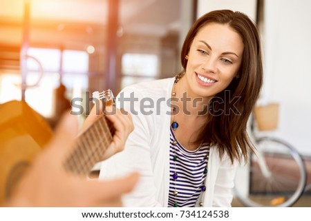 Young woman in office with friend playing guitar