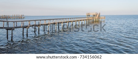 Fishing piers stretching out over Galveston Bay in Kemah, Texas, USA. Foot pier for saltwater fishing of vacation home/beach house rental/bay home in Lighthouse District waterfront at sunset. Panorama