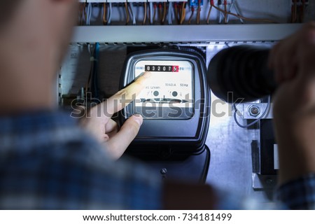 Person's Finger Pointing To Electric Meter Reading Using Flash Light Royalty-Free Stock Photo #734181499