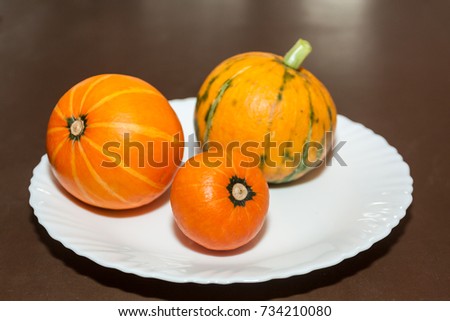 Three small orange pumpkins on white plate on brown table