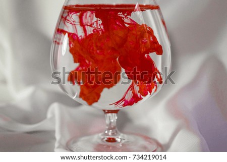 Red watercolor in a glass. Color mix in the glass. Paint in water. Colorful cocktail.