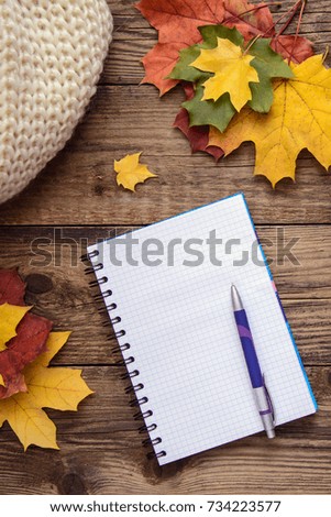 Beautiful autumn picture with a notebook and pen, yellow, orange, red, green leaves and scarf on wooden background