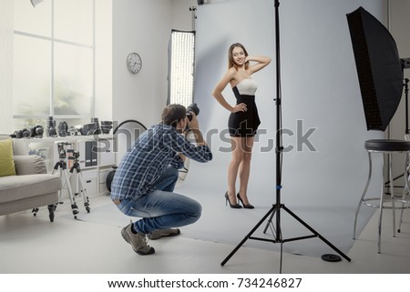 Young beautiful female model posing for a photo shoot in a studio, a photographer is shooting with a digital camera