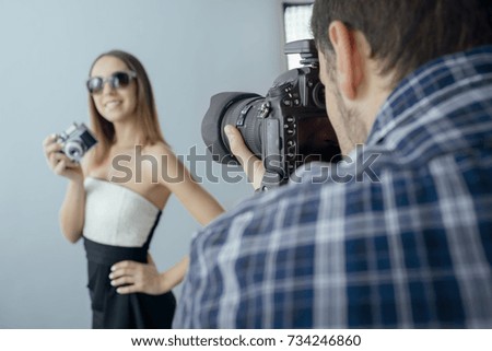 Beautiful female fashion model doing a photo shoot and posing with a vintage camera, a professional photographer is shooting with a dslr camera