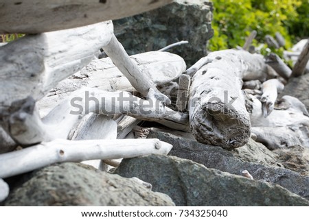 Side view close up on a pile of washed up driftwood logs, made pale by sun bleaching and weathering, on top of rock boulders on a Pacific Northwest beach