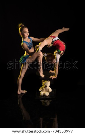 Two girls gymnasts athlete performs acrobatic elements on a black background in a yellow scenic light.