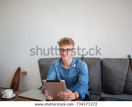 Young stylish hipster guy skilled freelancer working distance in internet via touch pad, sitting in coffee shop. Handsome man lifestyle writer using portable digital tablet, resting in recreation room