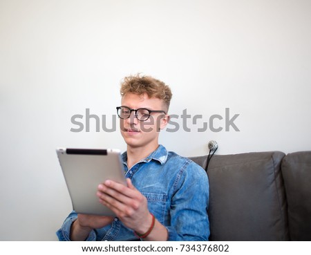 Young confident businessman watching financial news in internet via portable touch pad, sitting in office interior. Male in glasses successful website content creation working on digital tablet