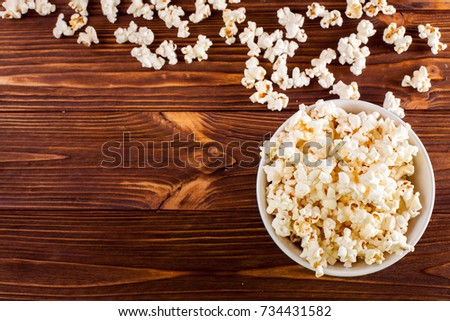 Popcorn banner -top view of paper cup and kernels lying on brown wooden background for cinema card or flyer with text area.
