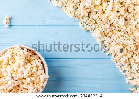 Popcorn banner - top view of paper cup and kernels lying on blue wooden background for cinema card or flyer with copy space.