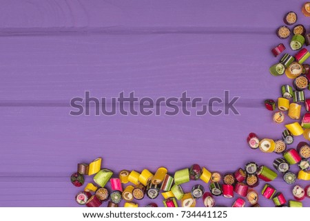 A corner frame made of colored caramel candies on wooden purple background. Copy space
