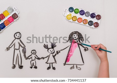 The child's hand paints a happy family with brush of watercolor on a white sheet of paper. The top view