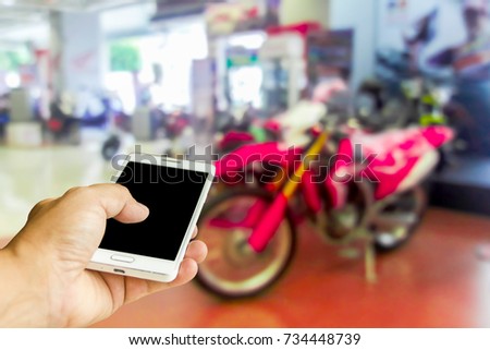 Man use mobile phone, blur image of motorcycle showroom as background.