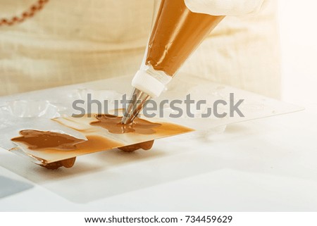 A close-up of a confectioner with a pastry syringe pours chocolate into a plastic bear form