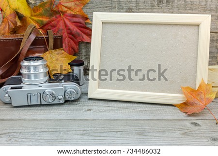 empty photo frame and vintage camera on grey wooden desk with vibrant fallen leaves