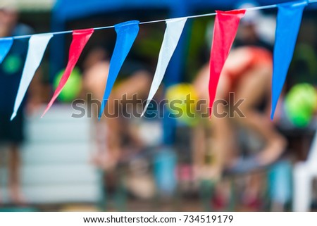 sport multi-color sling flags hanging over swimming pool, selective focus on the middle blur flag with blurred background of swimmers getting ready to start, sport or competition concept