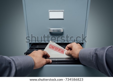 Office clerk searching for files in the filing cabinet, he finds a folder with confidential information inside, personal point of view Royalty-Free Stock Photo #734586823