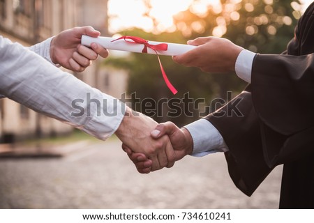 Cropped image of graduate in academic dress taking his diplomas and shaking hand Royalty-Free Stock Photo #734610241