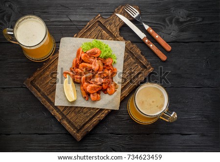 Grilled shrimps on a board and beer mug. Dark wooden table background.