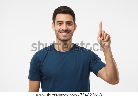 Attractive young man in blue t-shirt pointing up with his finger isolated on gray background Royalty-Free Stock Photo #734623618