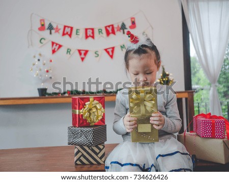 Asian little girl opening a magical Christmas gift in cozy living room in winter.