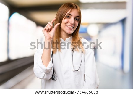 Young doctor woman making tiny sign in the hospital